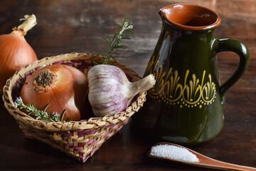 ingredients for organic food in a basket: garlic, onion, rosemary. Ceramic olive oil and wooden spoon with salt. on rustic wooden table.