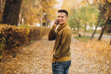 Portrait of handsome and happy guy smiling and talking on the phone in the autumn park