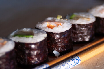 sushi in a row with chopsticks on a wooden base