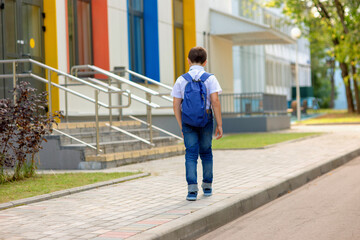 A brunette schoolboy in a white shirt, blue tie and blue backpack goes to school with colorful windows.