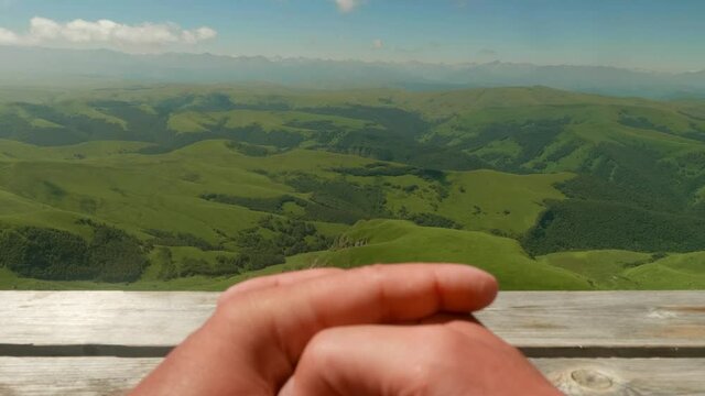 Veiw of man's hands at foreground on wooden surface and view of green plateau Bermamyth ahead. Tourist's impressions.