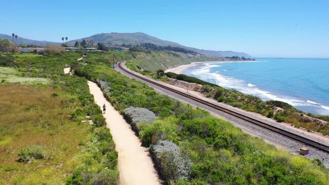 Aerial over man jogging runner exercise along coastal trail, railroad tracks and the Pacific coast near Carpinteria, Santa Barbara, California. 