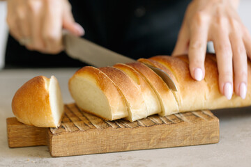 The process of cutting white bread on a wooden cutting board, hand movement, knife in hand.