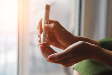 young woman hands using lancet on finger at home to check blood sugar level, diabetes concept,...