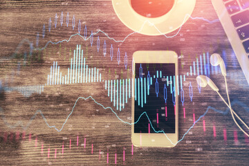 Double exposure of forex chart hologram over desktop with phone. Top view. Mobile trade platform concept.