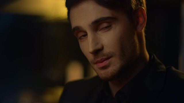 Charming guy raising eyebrows in dark background. Handsome man smiling indoors.