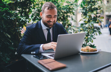 Cheerful entrepreneur browsing laptop at table in cafe