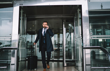 Caucasian businessman using mobile phone for calling after arrival to airport terminal, male lawyer with baggager using cellphone application for contact customer service and order cab taxi