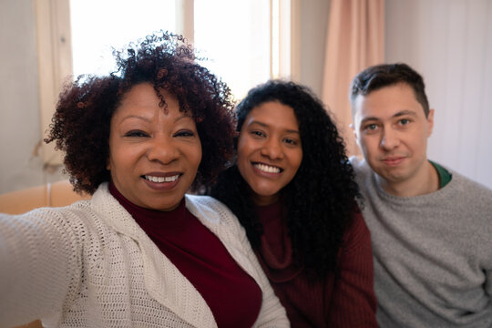 Portrait of brazilian african american womanwith daughter and son in lawtaking a self portrait. Inside the house in living room. Unity, happiness, affection, love, care concept..