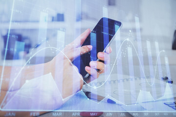 Double exposure of man's hands holding and using a digital device and forex graph drawing. Financial market concept.