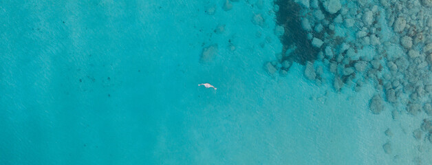 An aerial view of the beautiful Mediterranean Sea and a swimmer, where you can see the cracked rocky textured underwater corals and the clean turquoise water of Protaras, Cyprus,