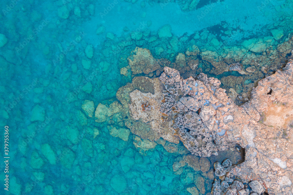 Wall mural An aerial view of the beautiful Mediterranean Sea, where you can see the cracked rocky textured underwater corals and the clean turquoise water of Protaras, Cyprus, - Wall murals