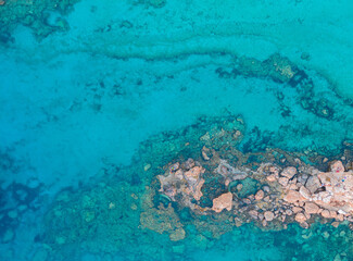 An aerial view of the beautiful Mediterranean Sea, where you can see the cracked rocky textured underwater corals and the clean turquoise water of Protaras, Cyprus,