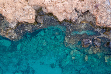 An aerial view of the beautiful Mediterranean Sea, where you can see the cracked rocky textured underwater corals and the clean turquoise water of Protaras, Cyprus,