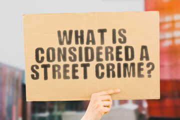 The question " What is considered a street crime? " on a banner in men's hand with blurred background. Street. Attack. Violation. Criminal crime. Stealing. Dangerous. Insecure. Unsafe