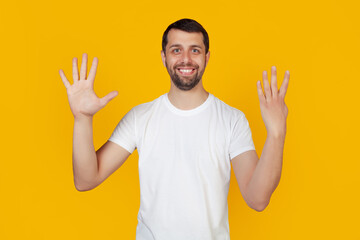 Modern young man with a beard in a white tank top shows number nine with fingers on hand smiling confidently and happily looking into the camera. The man shows nine fingers. Number 9 yellow background