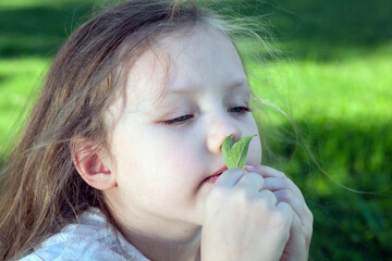 little girl in a white dress holds leaves on a green background closeup