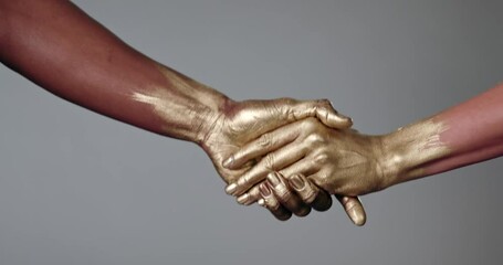 Close up of two hands painted in gold, coming to gather to shake.