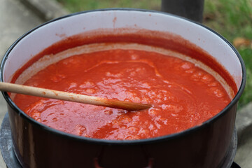 Close up on big pot with wooden spoon stirring hot ketchup or tomato sauce or soup while cooking...
