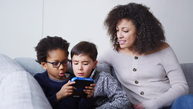 Mother and sons sitting on sofa at home playing computer game together on hand held device at home - shot in slow motion