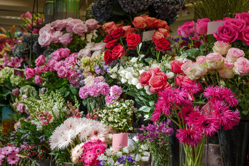 Fototapeta na wymiar Moody dark tone. Selected focus view at pale orange, pink and white bouquet of blooming roses and flowers in front of floral shop in outdoor market in Europe. Typical atmosphere of flower store. 