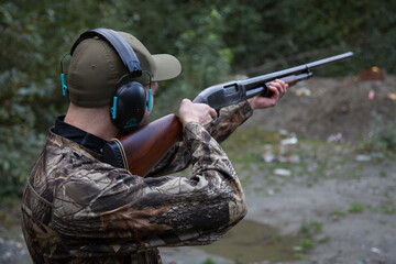 A man dressed in camo is aiming an old, wooden stock shotgun downrange ready to pull the trigger in...