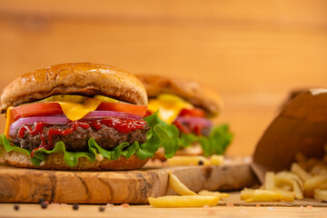 The big ruddy tasty burger with cheese, bacon, lettuce, steak and french fries on the wooden board isolated on beige background. Fast food.