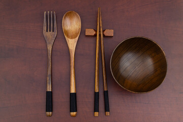 Wooden chopsticks, fork and spoon with bowl on wooden table