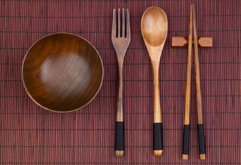 Wooden fork, spoon, chopsticks and bowl on bamboo place mat 