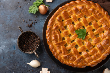 The big round tasty ruddy pie with mushrooms on the black plate isolated on dark background. The bowl with black pepper. garlic and champignouns are for decoration. Food concept. Cooking at home.