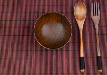 Wooden fork, spoon and bowl on bamboo place mat 