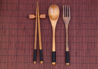 Wooden fork, spoon and chopsticks on bamboo place mat 