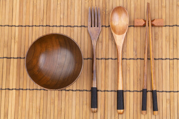 Wooden chopsticks, fork, spoon and bowl on bamboo place mat 