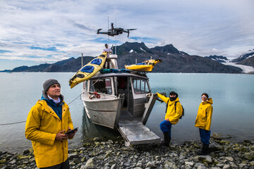 Man with crew members from scientific expedition  send a drone near the vessel docked on iceberg...