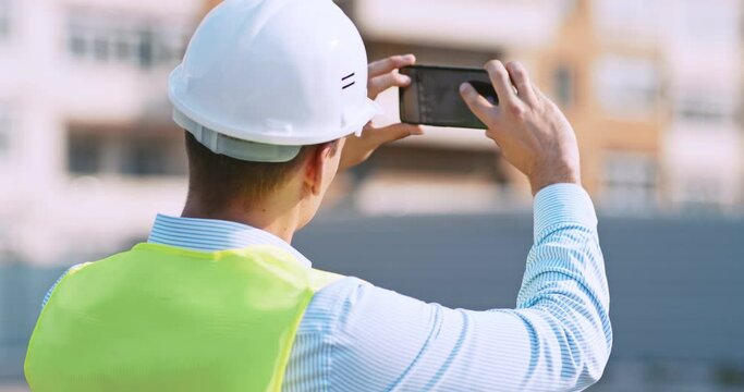 Worker at construction site making photos on his cell phone, back view, tracking shot