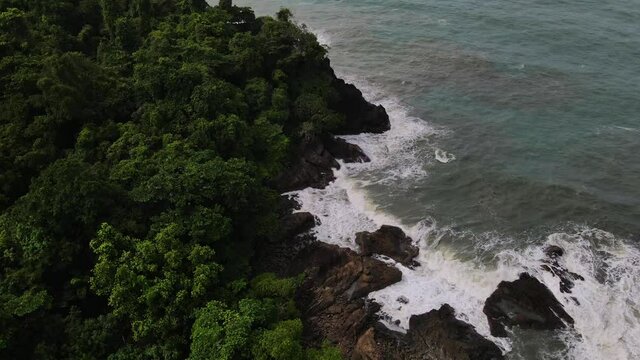 Aerial view above exotic islands treetop canopy and coastal splashing surf landscape Thailand