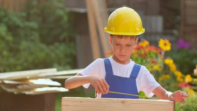 Little boy child future engineer builder architect with instruments, in uniforms, yellow helmet holding wooden board outdoors. Future kid children profession, big dream, building work, 4 K slow-mo
