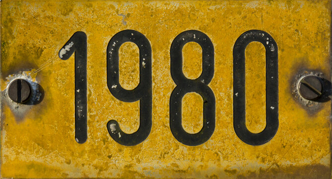 Gelbes verwittertes Schild mit Jahreszahl 1980