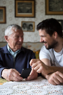 Adult grandson explaining to his granddad how to use a smartphone