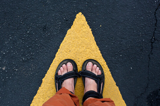 A woman's feet standing on the tip of a yellow arrow painted on