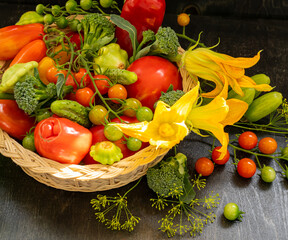 Harvest different types of fresh tomatoes, cucumbers, squashes and zucchini close-up in a wicker basket on a black table