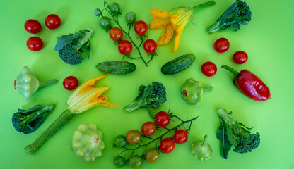 Layout of colorful organic vegetables,  from above on a green background. The ingredients for cooking are tomatoes, cucumbers, broccoli, red peppers, and squashes. Top view