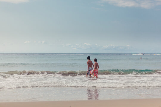 Two boys in swimming shorts walking into the ocean in the summer