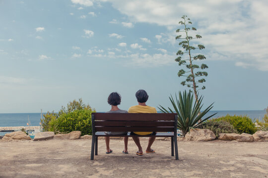 Father and son sitting on a bench overlooking the ocean on a summer day