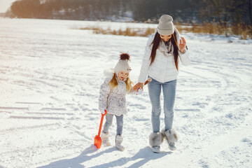 Fototapeta na wymiar young and stylish mom with long dark hair playing with her little cute daughter in winter snow park