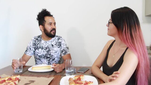 Joven pareja de mexicanos platicando y comiendo pizza en casa 