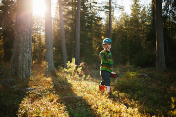 Little boy with red boots standing in the forest.