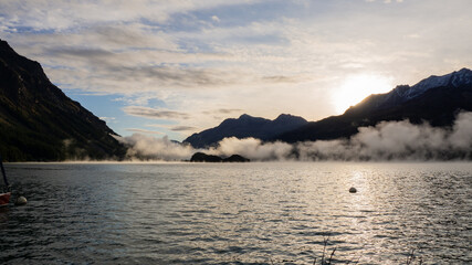 Fototapeta na wymiar Maloja mountain Pass, Switzerland. Landscape of the lake Sils in the morning during the fall time. The fog covers the lake and the shores. Traditional Swiss contest. Natural landscape