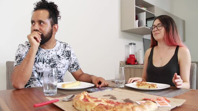Joven pareja de mexicanos platicando y comiendo pizza en casa discutiendo 