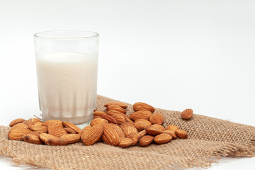 Organic white almond milk in a glass  with whole almonds spilled over a white table. Focus on nutmilk with blurred background.